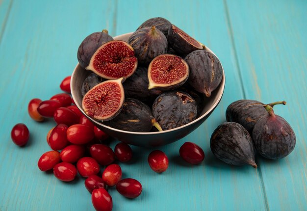 Top view of sweet ripe black mission figs on a bowl with cornelian cherries isolated on a blue wooden wall