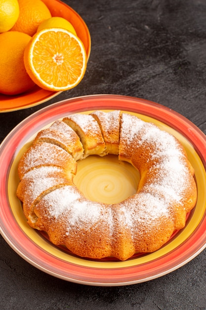 A top view sweet round cake with sugar powder sliced sweet delicious inside plate along with oranges and on the grey background biscuit sugar cookie