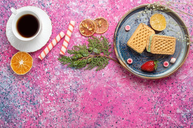 Top view of sweet waffles with cup of tea on light-pink surface