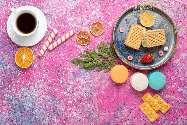 Top view of sweet waffles with cup of tea on the light-pink surface