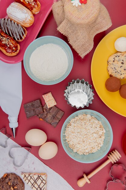 빨간 테이블에 계란 귀리 플레이크와 밀가루 케이크 쿠키 초콜릿으로 과자의 상위 뷰