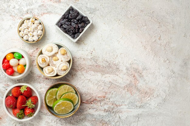 Top view sweets in bowls bowls of appetizing berries dried pineapples and other sweets on the white table