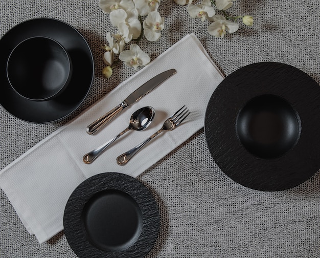 Вид сверху сервировки стола на поверхности гей с пустыми черными тарелками и серебряной ложкой вилкой и ножом