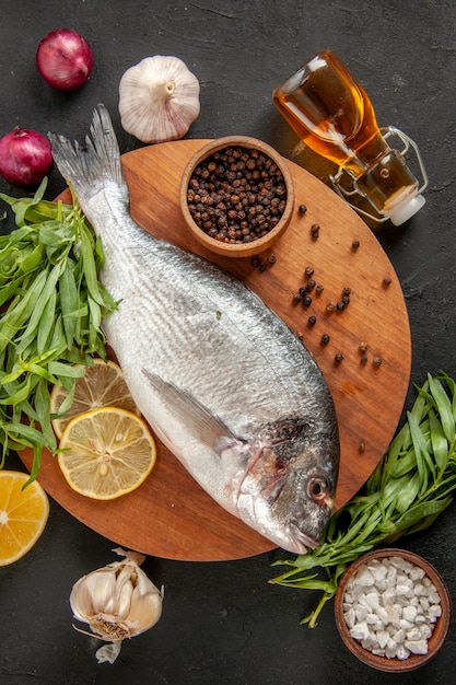 Top view tarragon fresh raw fish black pepper bowl on round wood board oil bottle garlic red onion on black