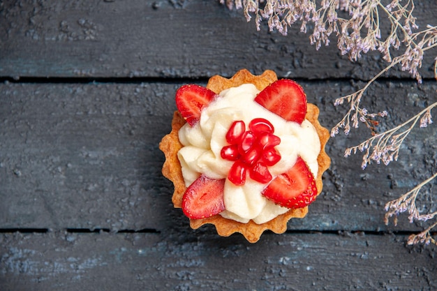 Top view tart with strawberry and pomegranate dried flower branch on dark surface