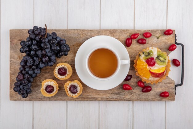 Top view tartlets with a cup of tea  black grapes and dogwood on a cutting board