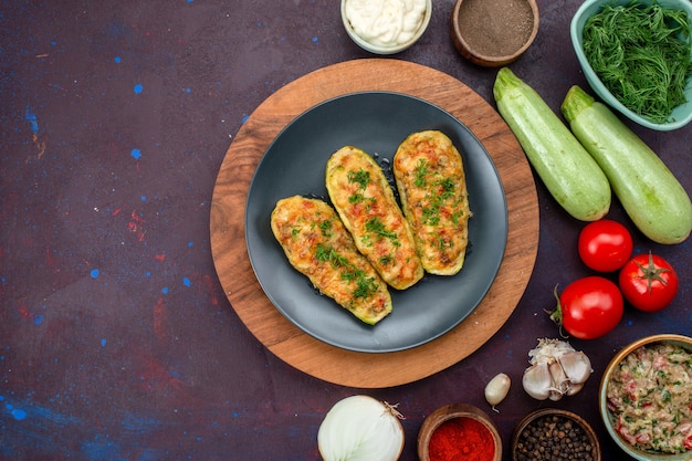 Top view of tasty baked squashes with greens along with fresh vegetables and seasonings on dark surface