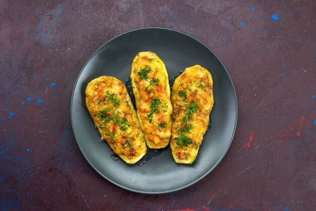 Top view of tasty baked squashes with greens inside plate on dark surface