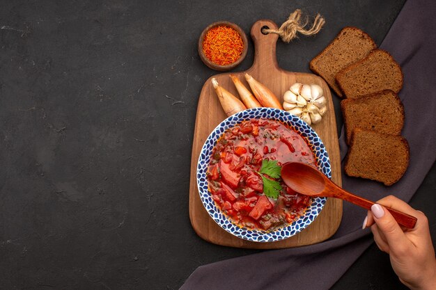 Top view tasty borsch ukranian beet soup with dark bread loafs on a dark space