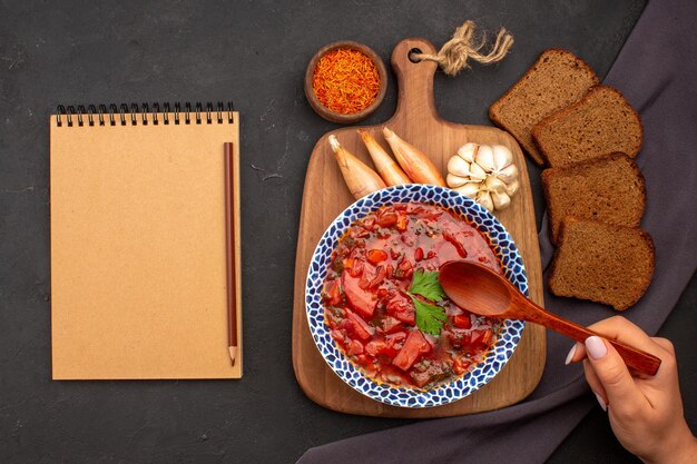 Top view tasty borsch ukranian beet soup with dark bread loafs on the dark space