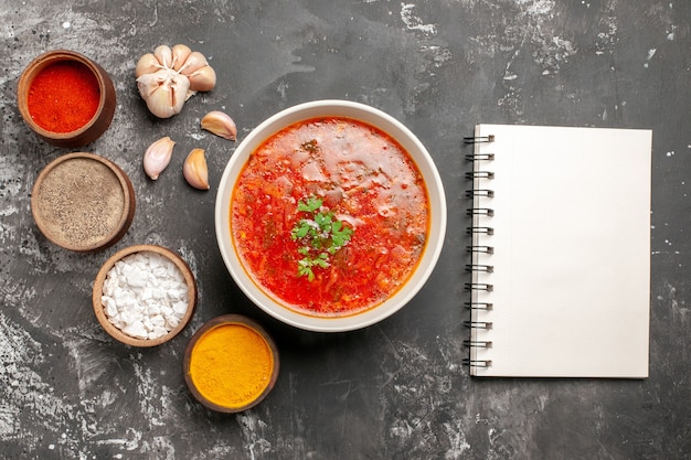 Top view of tasty borsch with seasonings on a dark surface