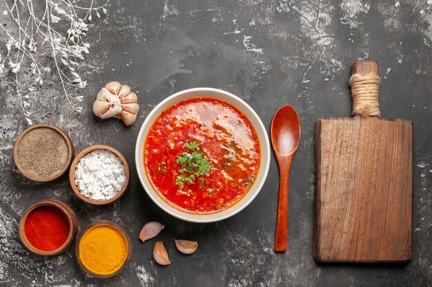 Top view of tasty borsch with seasonings on dark surface