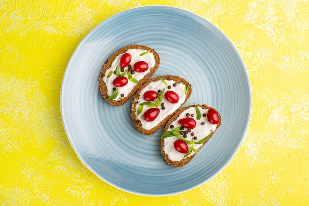 Top view of tasty bread toasts with sour cream and dogwoods inside blue plate on the yellow floor