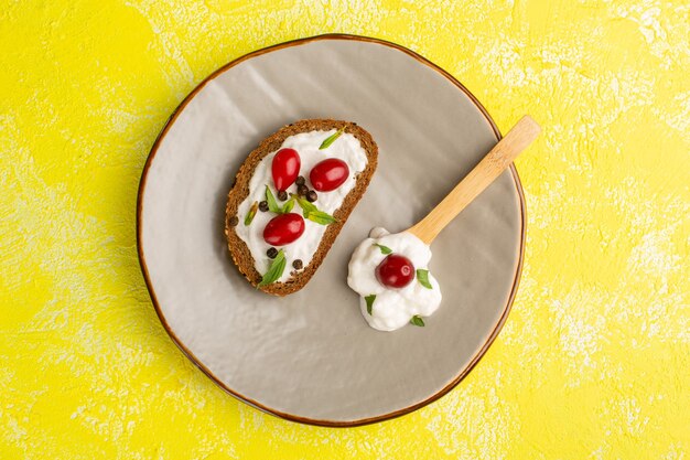 Top view of tasty bread toasts with sour cream and dogwoods inside plate on the yellow surface