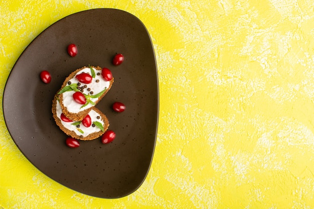Top view of tasty bread toasts with sour cream and dogwoods on the yellow surface