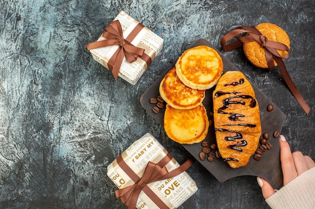 Top view of tasty breakfast with pancakes croisasant stacked cookies beautiful gift boxes on dark surface