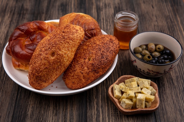 Top view of tasty buns on a plate with olives and chopped slices of cheese on a wooden background