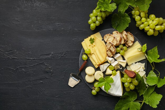 黒い石の上の円形のキッチンプレートにフルーツ、ブドウのおいしいチーズプレートの上面図