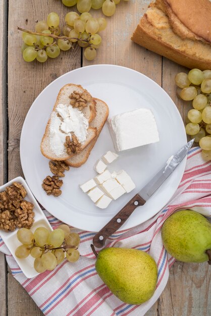 Вид сверху вкусного сыра на ломтик хлеба с виноградом и грушей