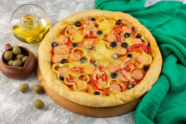 Вид сверху вкусной сырной пиццы с сосисками из черных оливок и красными помидорами вместе с маслом на сером столе, фаст-фуд, выпечка из итальянского теста