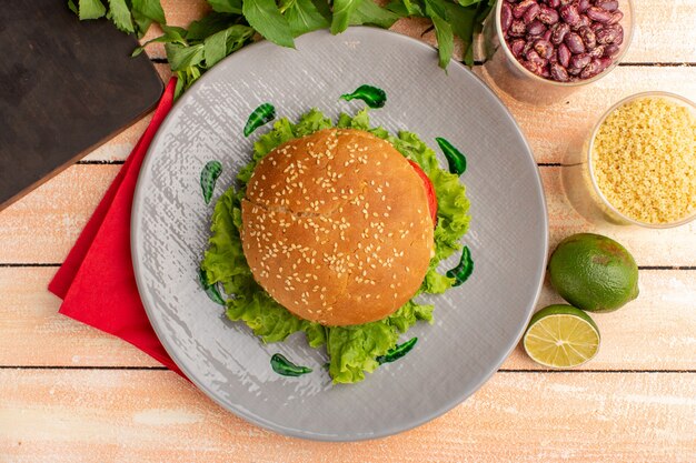 Top view of tasty chicken sandwich with green salad and vegetables inside plate on the wooden cream surface