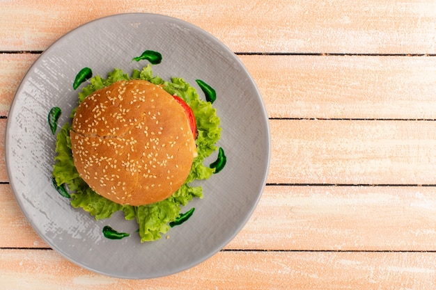 Vista dall'alto del gustoso panino al pollo con insalata verde e verdure all'interno del piatto sulla superficie crema rustica in legno