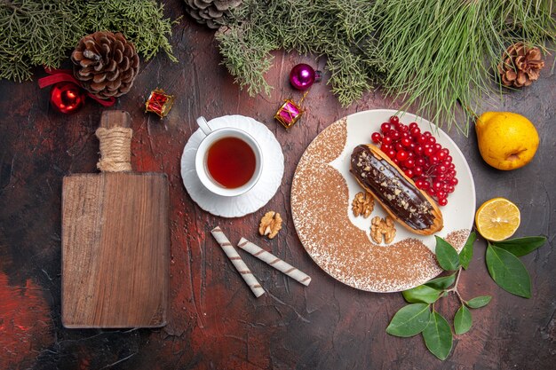 Top view tasty choco eclairs with red berries and tea on dark table pie cake dessert sweet