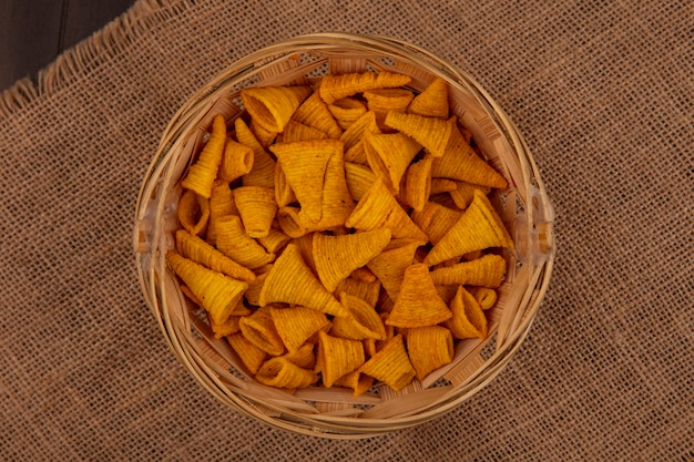 Top view of tasty cone shape fried corn snacks on a bucket on a sack cloth on a wooden table