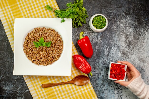 Вид сверху вкусной приготовленной гречки с зеленью и болгарским перцем на светло-сером столе