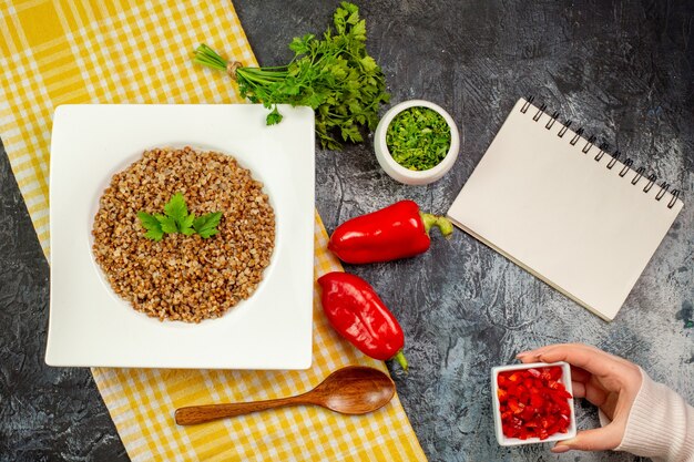 Top view tasty cooked buckwheat with greens and bell-peppers on light-grey table