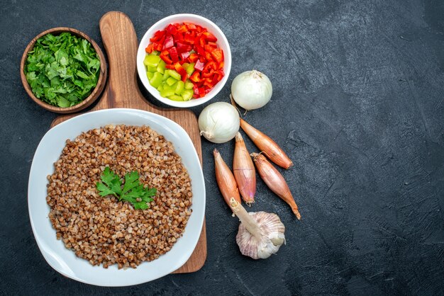 Top view tasty cooked buckwheat with greens and vegetables on grey