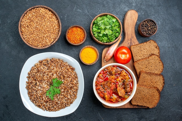 Free photo top view tasty cooked buckwheat with seasonings and bread loafs on grey