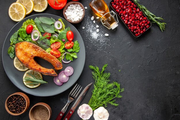 Top view tasty cooked fish with fresh vegetables on dark table