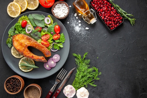 Вид сверху вкусной приготовленной рыбы со свежими овощами на темном столе