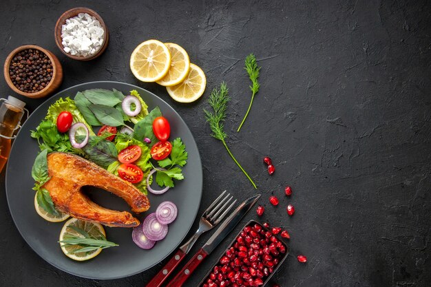 暗いテーブルの上に新鮮な野菜とおいしい調理された魚の上面図