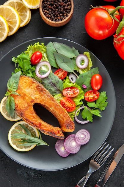 Top view tasty cooked fish with fresh vegetables and lemon slices on dark table