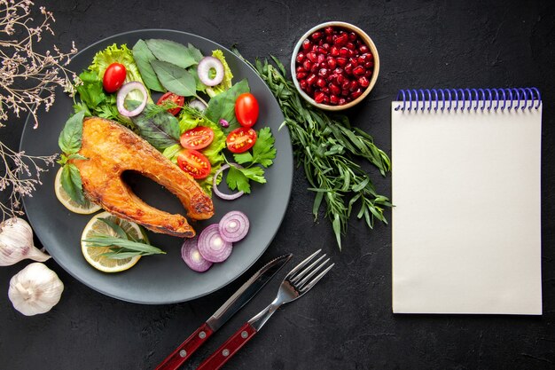 Top view tasty cooked fish with fresh vegetables and seasonings on dark table