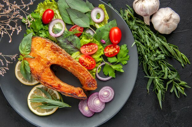 Top view tasty cooked fish with fresh vegetables and seasonings on dark table