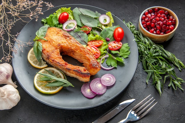 Вид сверху вкусной приготовленной рыбы со свежими овощами и приправами на темном столе