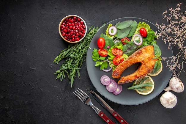 Вид сверху вкусной приготовленной рыбы со свежими овощами и приправами на темном столе