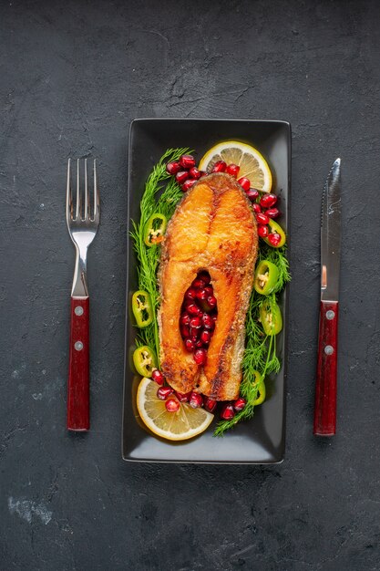 暗いテーブルの鍋の中に緑とレモンのスライスとおいしい調理された魚の上面図