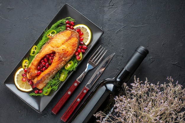 Top view tasty cooked fish with greens and lemon slices inside pan on dark table