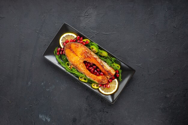 Top view tasty cooked fish with greens and pomegranates inside pan on dark table