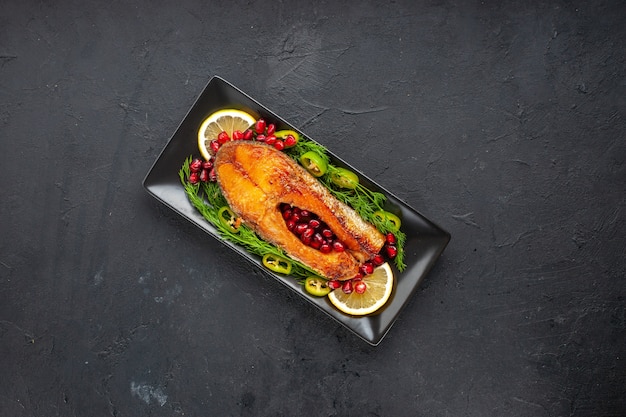 어두운 탁자에 있는 팬 안에 채소와 석류를 넣은 맛있는 요리된 생선