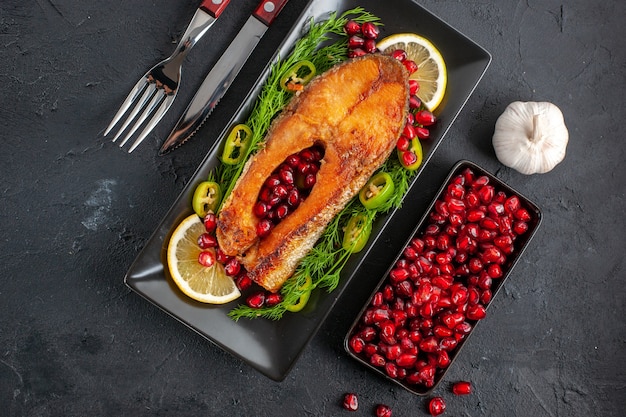 Top view tasty cooked fish with lemon greens and pomegranates