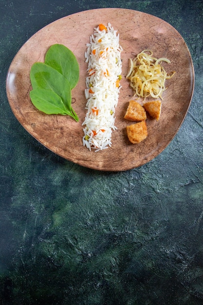 Вид сверху вкусный приготовленный рис с зелеными листьями, фасолью и мясом внутри тарелки на темном столе