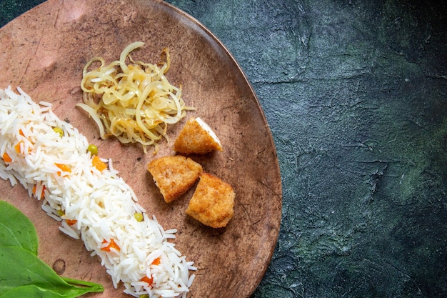 Вид сверху вкусный приготовленный рис с зелеными листьями, фасолью и мясом внутри тарелки на темном столе