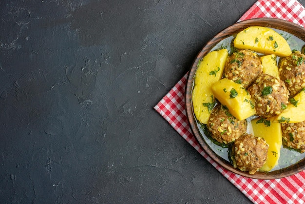 Top view of tasty dinner with meatballs potatoes green in a brown bowl on red stripped towel on black background with free space