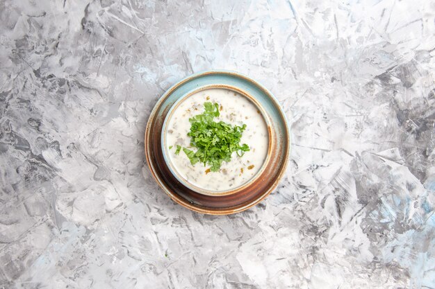 Вид сверху вкусный йогуртовый суп довга с зеленью внутри тарелки на белом столовом молочном супе