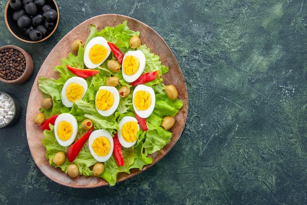 вид сверху вкусный яичный салат с зеленым салатом, оливками и приправами на темно-синем фоне